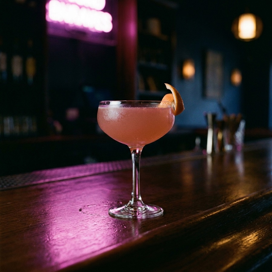 Cocktail rose en coupe sous la lueur néon magenta